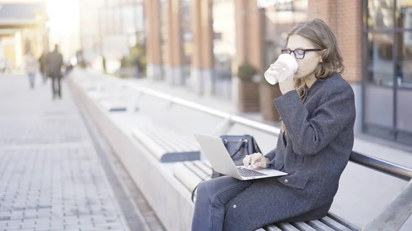 Genç işkadını kahve içme bir dizüstü bilgisayar ile şehir — Stok fotoğraf
