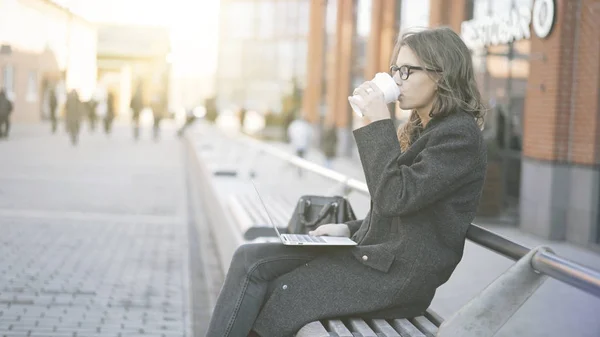 Joven mujer de negocios con un ordenador portátil bebiendo café, calle — Foto de Stock