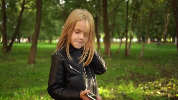 Дівчина в шкіряній куртці слухає музику в парку — стокове відео