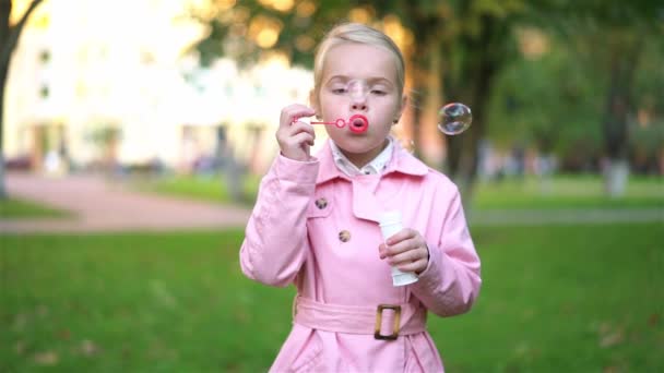 Linda niña en rosa jugando con burbujas de jabón afuera — Vídeo de stock