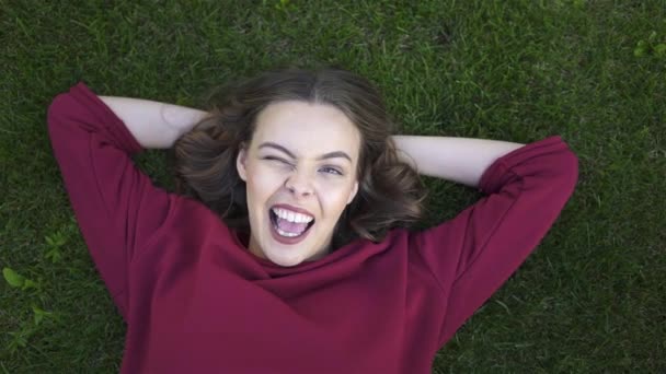 Top view of young woman lying on grass and winking — Stock Video
