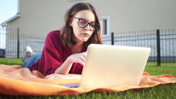 Συμπυκνωμένο κορίτσι με τα γυαλιά που βρίσκεται στην αυλή της με έναν φορητό υπολογιστή — Αρχείο Βίντεο