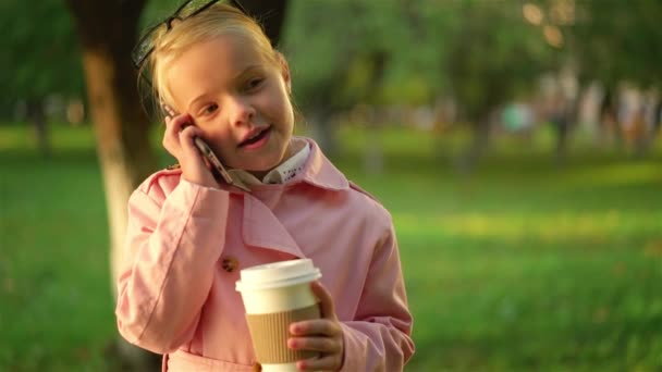 Menina bonito em rosa falando ao telefone e segurando um café — Vídeo de Stock