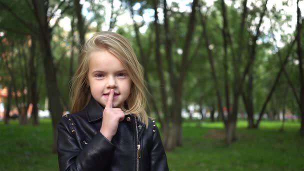 Милая маленькая девочка делает знак молчания в парке — стоковое видео