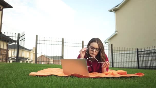 Chica en rojo acostado en su patio trasero con un ordenador portátil y auriculares — Vídeo de stock
