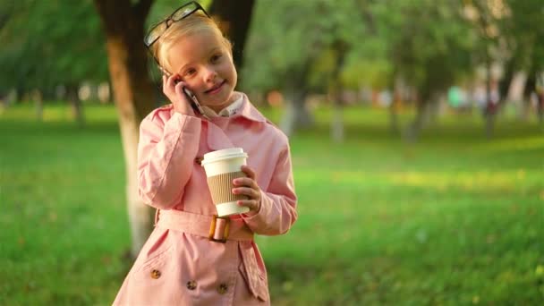 Liten flicka pratar telefon och hålla en kaffe — Stockvideo