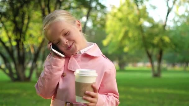 Malá holčička mluví o telefonu a drží na kávu, procházky v parku — Stock video