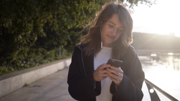 Mujer joven y relajada escuchando música y caminando cerca de un río — Vídeo de stock