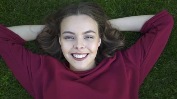Zoom out of young woman lying on grass and winking — Stock Video