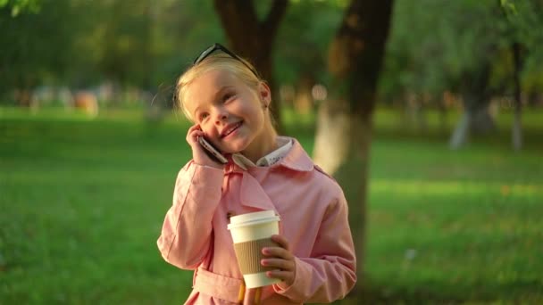 Pembe gülümseyen ve park telefonda konuşurken sevimli küçük kız — Stok video