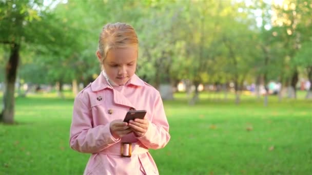 Little girl texting while walking in a park — Stock Video