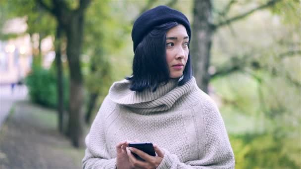 Beautiful Asian woman with a smartphone in an autumn park — Stock Video