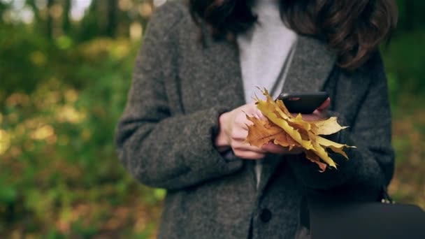 Невпізнавана молода жінка зі смартфоном в осінньому лісі — стокове відео