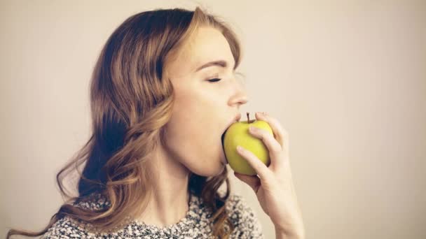 Mujer de pelo claro mordiendo una manzana verde y mirando la cámara tonificada — Vídeo de stock