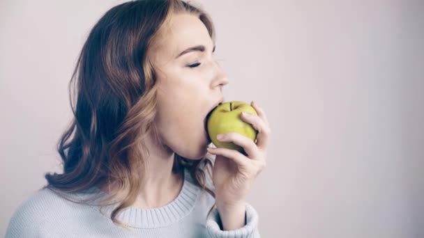 Красивая женщина кусает зеленое яблоко и смотрит в камеру — стоковое видео