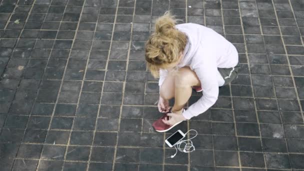 Вид зверху на жінку-бігунку, що зв'язує її шнурок і починає бігати надворі — стокове відео