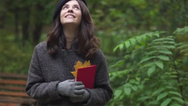 Happy brunette woman with a book smiling under a foliage — Stock Video