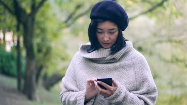 Attractive Asian woman looking at her smartphone in an autumn park — Stock Video