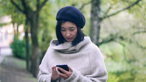 Привлекательная азиатка со смартфоном в осеннем парке — стоковое видео