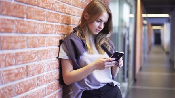 Atractiva joven mujer mensajes de texto en un pasillo de ladrillo — Vídeos de Stock