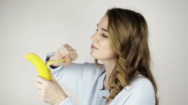 Hermosa joven pelando un plátano y comiéndolo — Vídeos de Stock