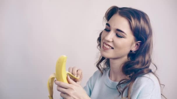 Mooie vrouw in grijze peeling en eten van een banaan — Stockvideo