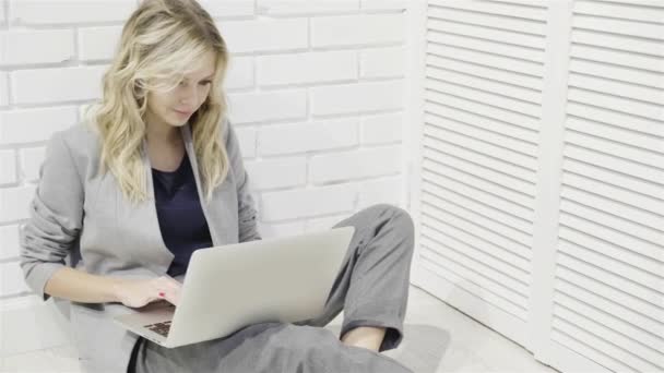Hübsche junge Frau in grau tippt auf Laptop auf dem Fußboden — Stockvideo