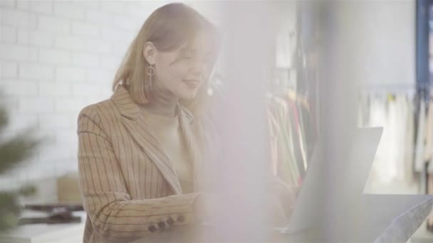 Mladá manažerka v béžové psát na svém notebooku v malé oblečení shop — Stock video