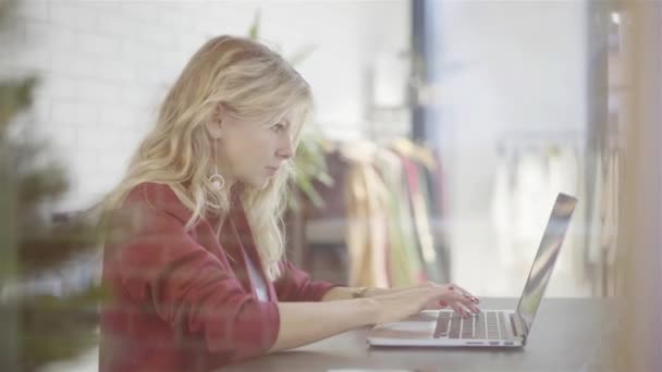 Unga föreståndarinnan att skriva på hennes laptop i en liten klädaffär — Stockvideo