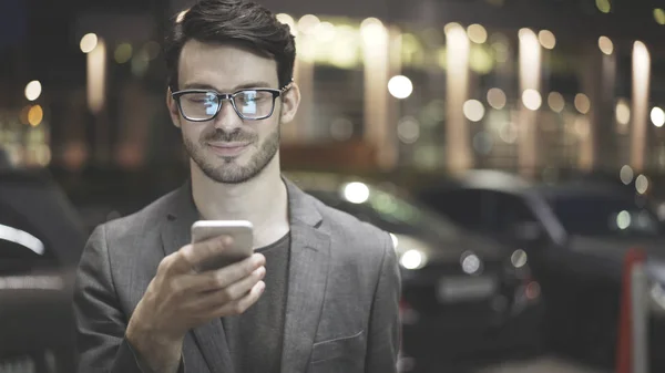 Усміхнений чоловік тримає і дивиться на свій мобільний телефон на вулиці — стокове фото