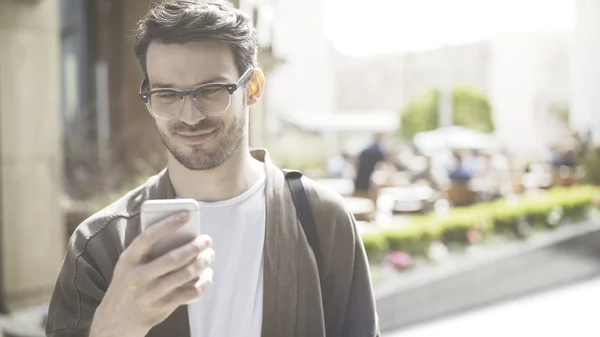 Молодий усміхнений чоловік прокручує телефон на вулиці — стокове фото
