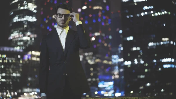 Un joven hombre de negocios con gafas vestidas con un traje negro por la noche — Foto de Stock