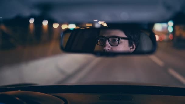 Young businessman driving his car in a night city, rear view mirror reflection — Stock Video