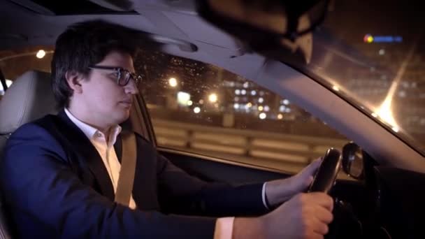 Jovem empresário de óculos dirigindo um carro em uma cidade noturna — Vídeo de Stock