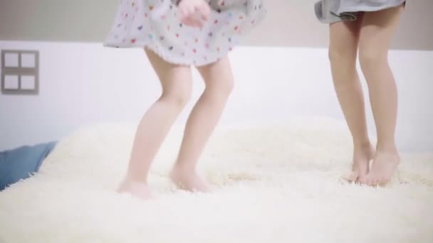 Duas meninas irreconhecíveis em vestidos pulando em uma cama grande — Vídeo de Stock