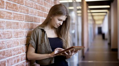 Genç gülümseyen güzel bir kız bir tablet tutan duvara duruyor
