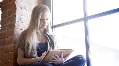 Genç kadın pencere pervazına üzerinde otururken dijital tablet kullanma