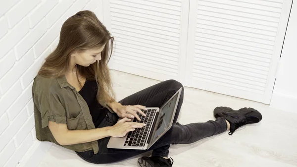 Bir genç gülümseyen güzel model kız öğrenci duvara katta oturan dizüstü bilgisayar ile çalışma — Stok fotoğraf
