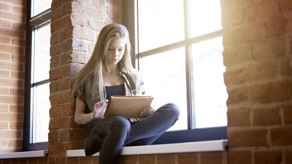 Jovem mulher usando tablet digital enquanto está sentado no peitoril da janela — Fotografia de Stock