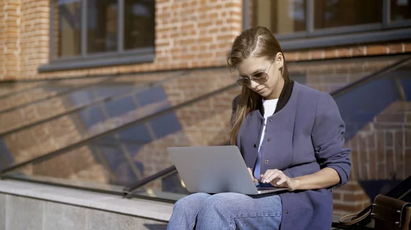 Güneş gözlüklü genç güzel bir kız ile bir dizüstü bilgisayar outisde çalışıyor — Stok fotoğraf
