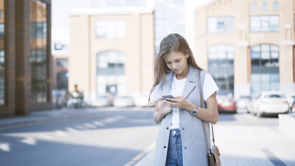 Een jong meisje alleen gekleed in een jas met een telefoon — Stockfoto