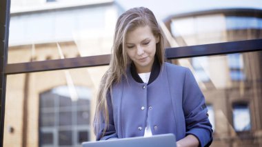 Bir genç gülümseyen kız bir dizüstü bilgisayarda yazarak bir eşiğinde oturuyor