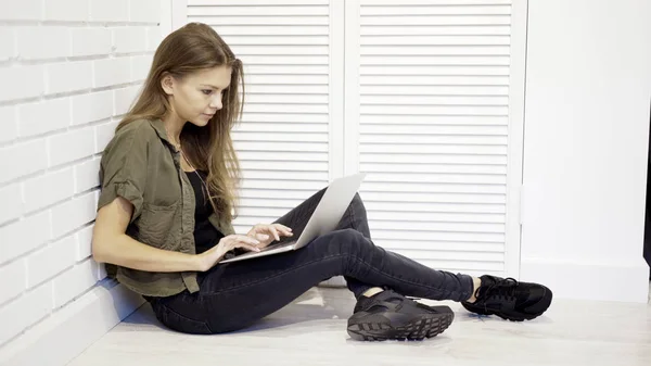 Una giovane studentessa concentrata sta lavorando con un computer portatile seduto sul pavimento — Foto Stock
