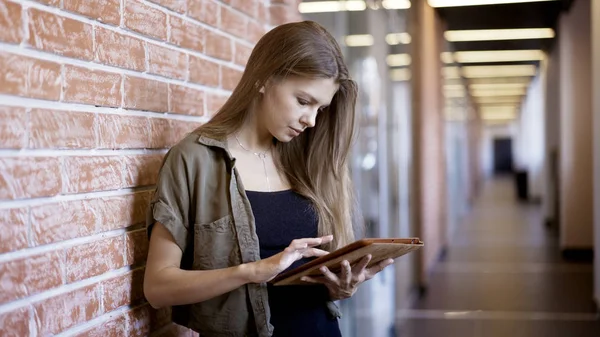 Een vrij ernstige meisje staat tegen de muur die houden van een tablet — Stockfoto