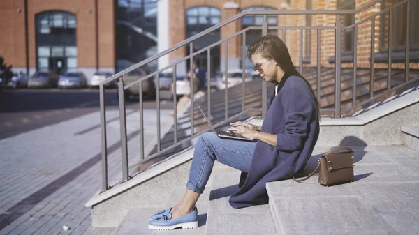 Een jong meisje in zonnebril is werken met een laptop outisde — Stockfoto