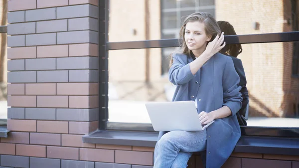 Een lachende meisje zit op een dorpel te typen in een laptop — Stockfoto