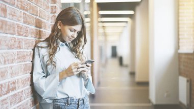 Genç kız koridor binada telefon bakarak