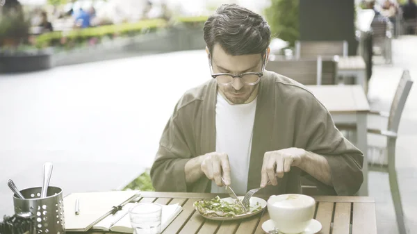 Un hombre guapo barbudo está comiendo ensalada en el café al aire libre solo. — Foto de Stock