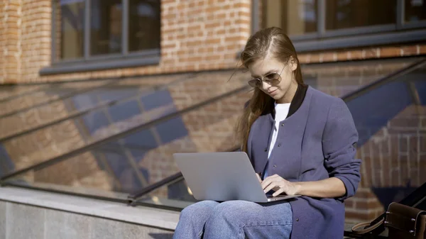 Güneş gözlüklü genç güzel bir kız ile bir dizüstü bilgisayar outisde çalışıyor — Stok fotoğraf