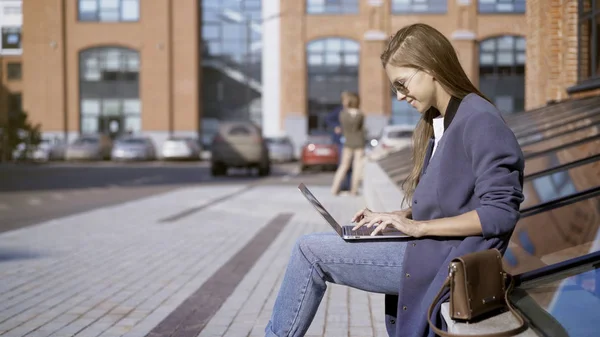 Een mooi meisje in zonnebril is werken met een laptop outisde — Stockfoto